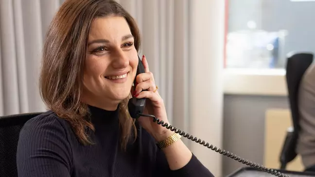 Žena telefonuje, zatiaľ čo sedí na pracovisku a usmieva sa