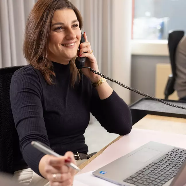 žena telefonuje, zatiaľ čo sedí na pracovisku a usmieva sa