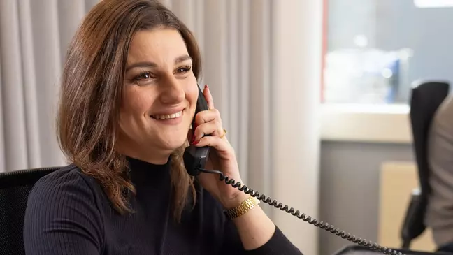 Žena telefonuje, zatiaľ čo sedí na pracovisku a usmieva sa