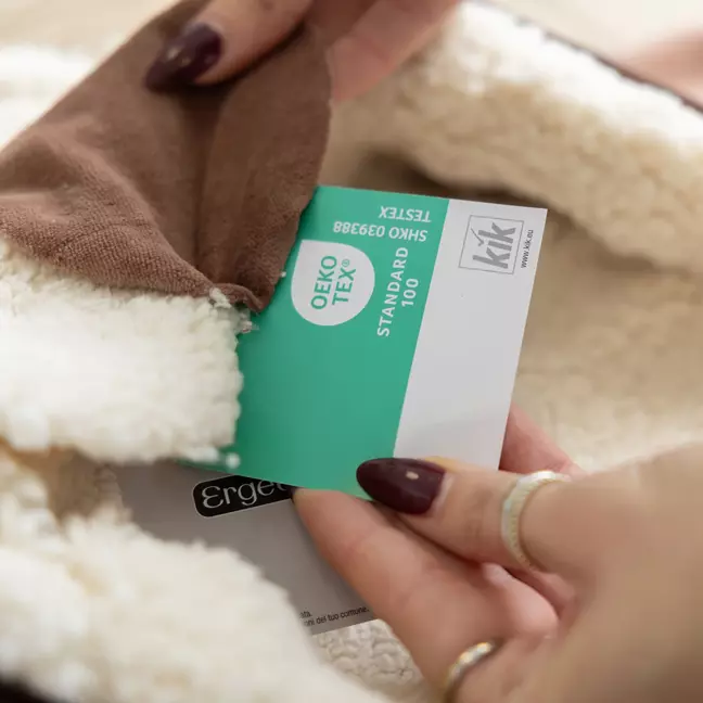 Osoba kontroluje vnútornú podšívku odevu a pritom drží v ruke certifikačnú etiketu OEKO-TEX® Standard 100 s logom KiK
