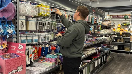 Ein Mann steht vor einem Schreibwaren-Regal und räumt Produkte ein.