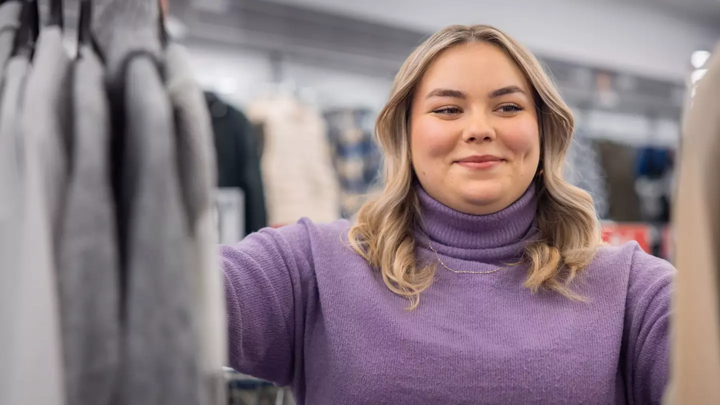 Eine Frau schaut auf Kleidungsstücke und lächelt dabei, sie steht in einer modernen Filiale