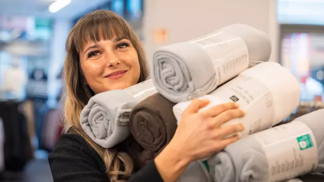 Predavačka stojí s úsmevom v predajni a v rukách drží veľa tovaru