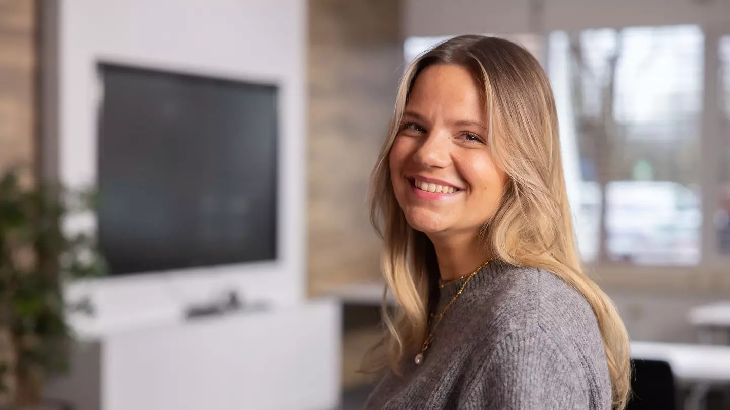 Žena sa s úsmevom pozerá do kamery, stojí v modernom interiéri
